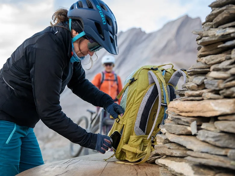 Outdoor Imagebild - Person mit Fahrradbekleidung und Fahrradhelm bedient ein Außenfach eines gelben Rucksacks.