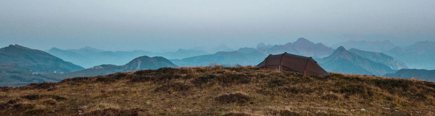 In den Bergen oberhalb der Baumgrenze ist ein Zelt aufgestellt. Es handelt sich um ein Zelt von Nordisk.