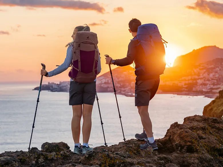 zwei Personen mit Rucksack bei Sonnenuntergang am Wasser