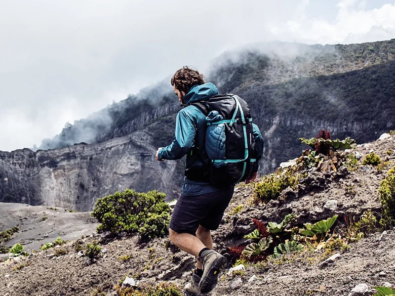 Outdoor Imagebild - Person im Gebirge mit einem blau schwarzen Rucksack bewegt sich schnell fort.