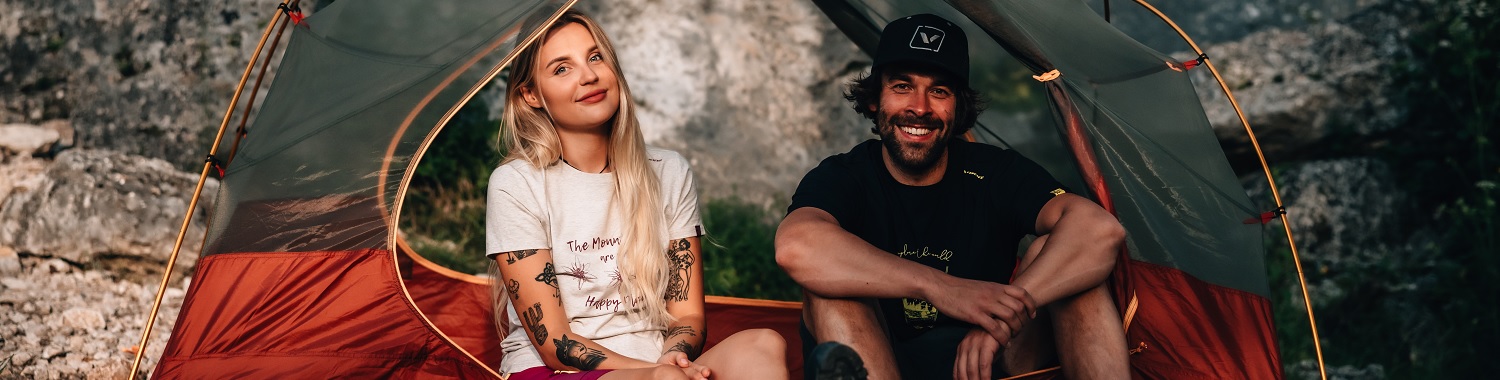 Zwei Personen sitzen in einem Zelt. Sie tragen Bambusshirts und sehen glücklich aus.