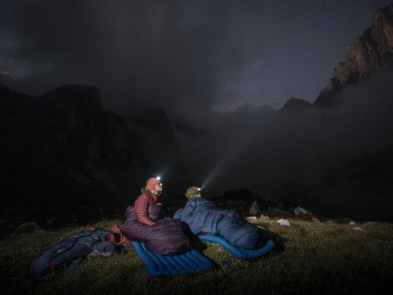 Outdoor Imagebild - zwei Personen übernachten im Freien auf Isomatten und in Outdoor Schlafsäcken. Zudem sind sie ausgerüstet mit Stirnlampen.