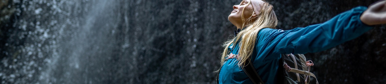 Person mit Hardshelljacke steht vor einem Wasserfall
