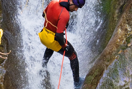 Person klettert mit Sicherheitsausrüstung wie Helm und Seil in einem Wasserfall