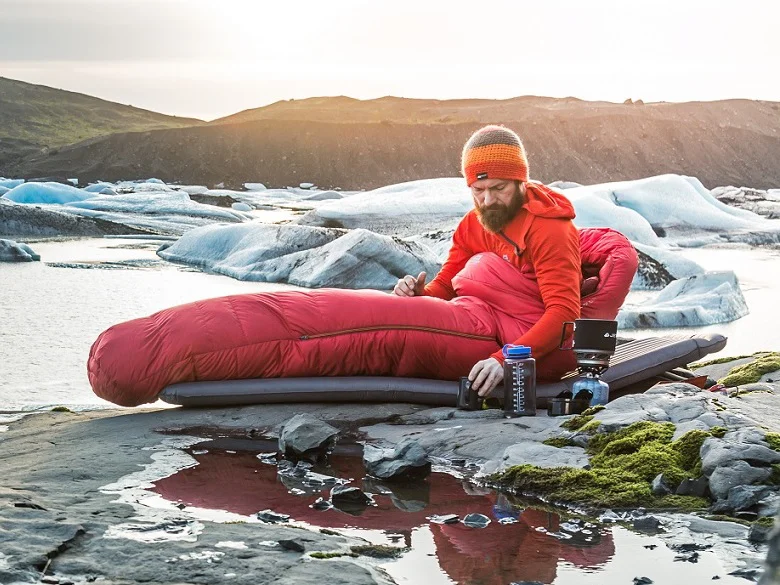 Outdoor Imagebild - Person im freien auf einer Isomatte in einem Schlafsack - in der Umgebung ist eine kalte Eislandschaft bzw. Felslandschaft